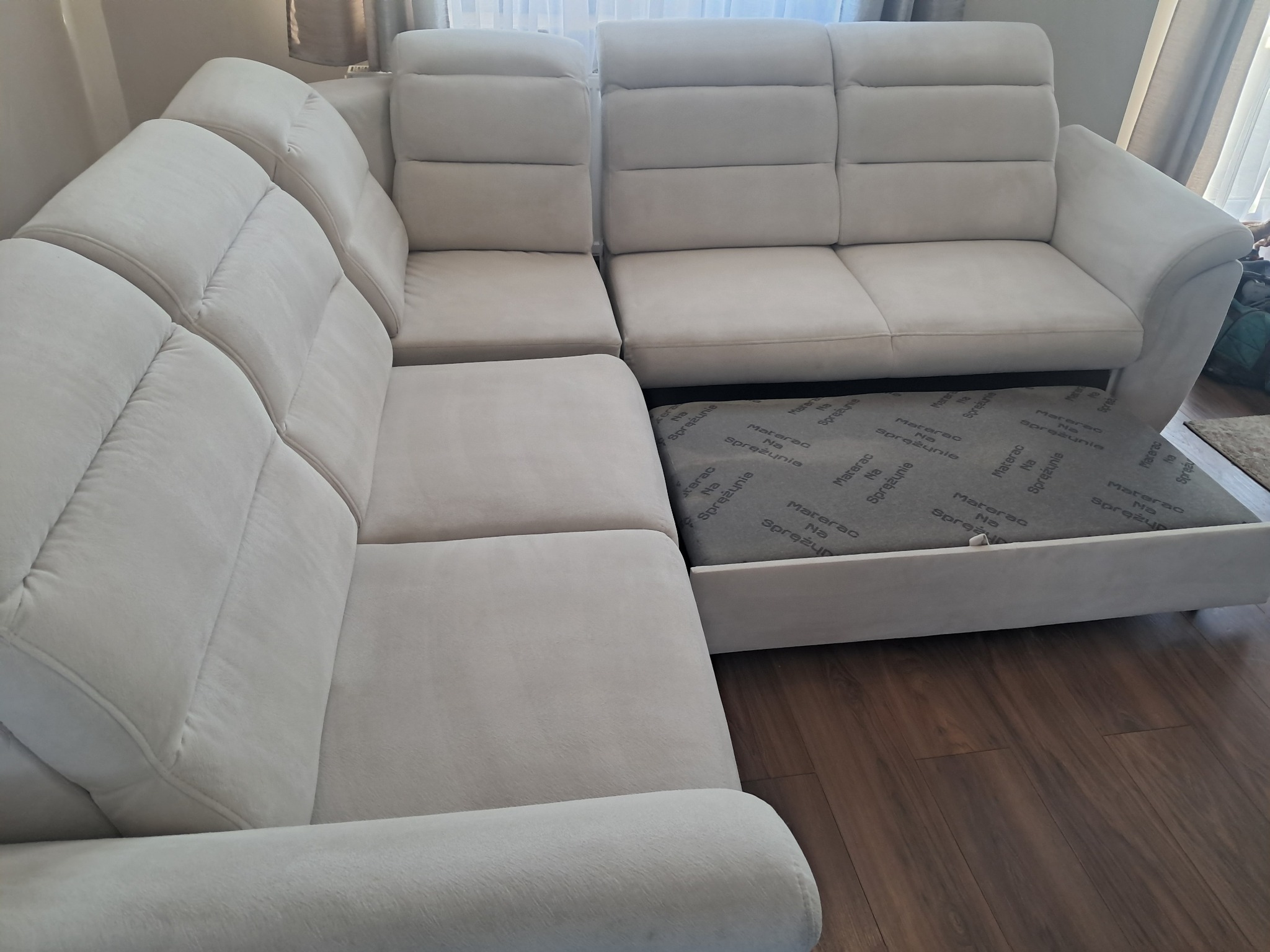 Jasny narożnik z wysuwanym materacem na sprężynach, po czyszczeniu. Widoczne detale tapicerki i konstrukcji, podkreślające świeżość i dokładność wykonanej usługi.