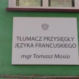 Tabliczka informacyjna na zielonej ścianie z napisem: Tłumacz Przysięgły Języka Francuskiego mgr Tomasz Mosio, nad napisem godło Polski.