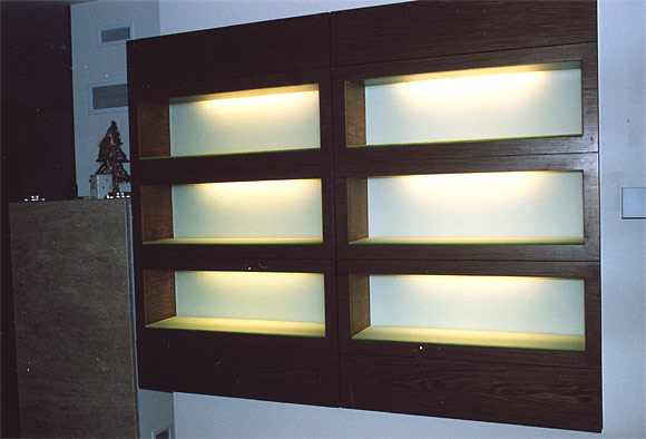 Ścianka działowa z ciemnego drewna z sześcioma podświetlanymi, pustymi wnękami o mlecznym szkle w tle, tworząca minimalistyczny element dekoracyjny wnętrza.