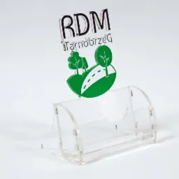Przezroczysty stojak na wizytówki z logo RDM Tarnobrzeg, z motywem drzew i drogi, na białym tle.