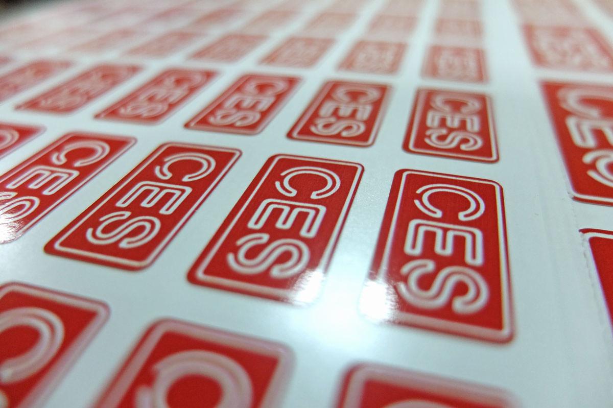 Arkusz z powtarzalnymi, prostokątnymi, czerwono-białymi etykietami z napisem 'CES', widoczne pod kątem z bliska.