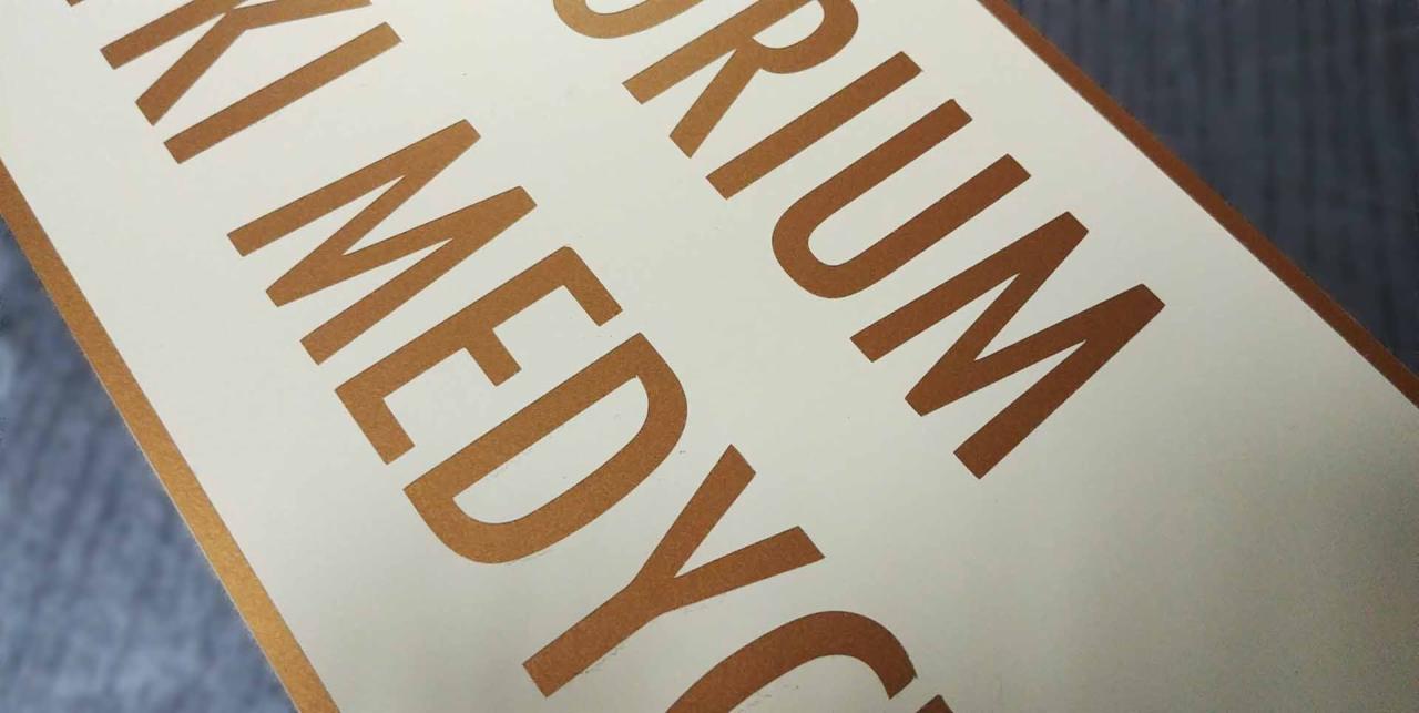 Zbliżenie na fragment druku z metalicznymi, miedzianymi literami na kremowym tle.