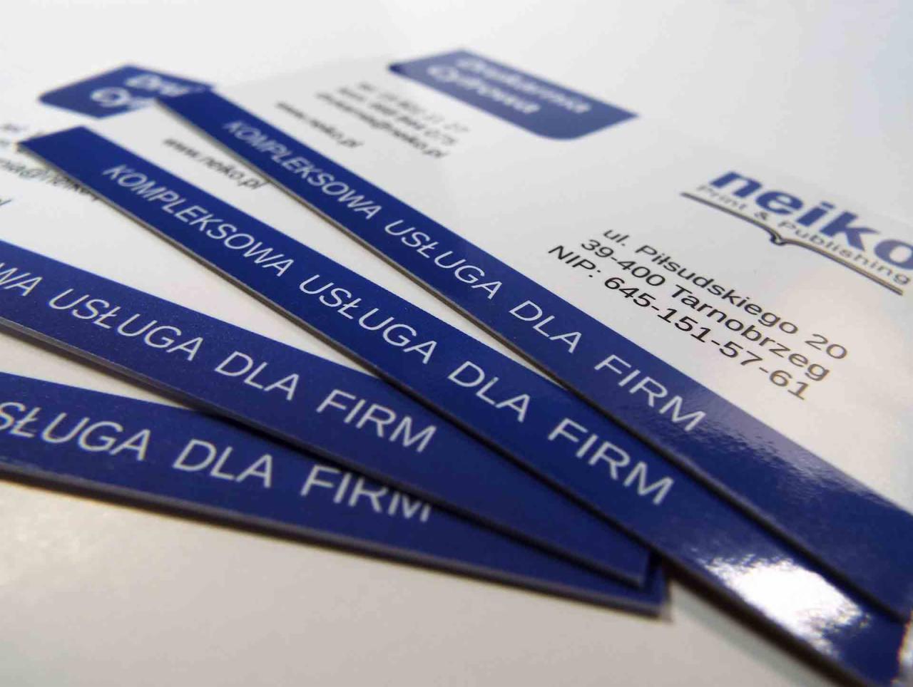 Stos wizytówek w odcieniach bieli i granatu z napisem 'Kompleksowa usługa dla firm' oraz danymi teleadresowymi drukarni Neiko z Tarnobrzegu.