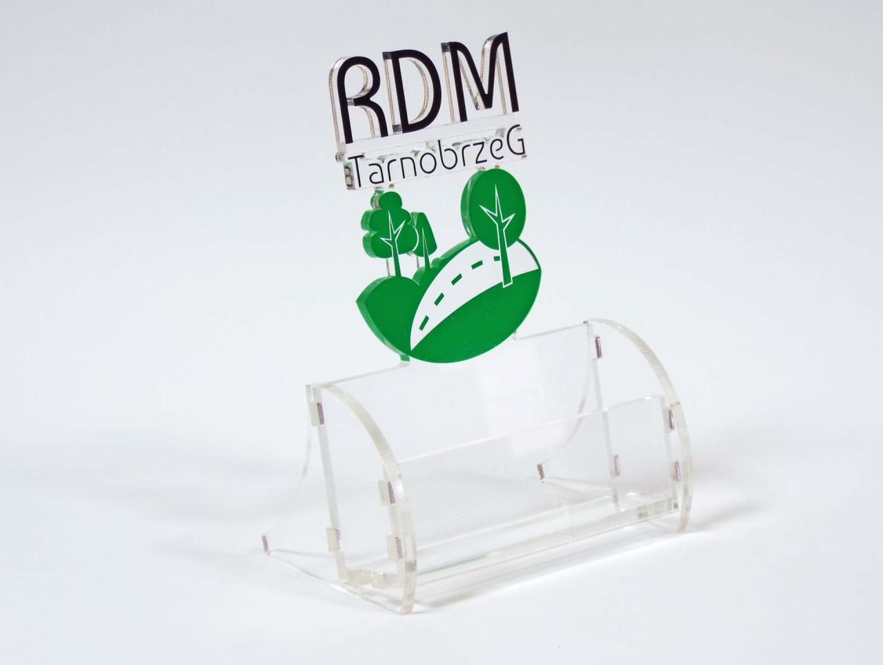 Przezroczysty stojak na wizytówki z logo RDM Tarnobrzeg, z motywem drzew i drogi, na białym tle.