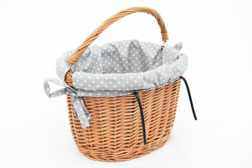 Wiklinowy koszyk rowerowy z szarą wyściółką w białe kropki, zawiązany z boku na kokardę, na białym tle.
