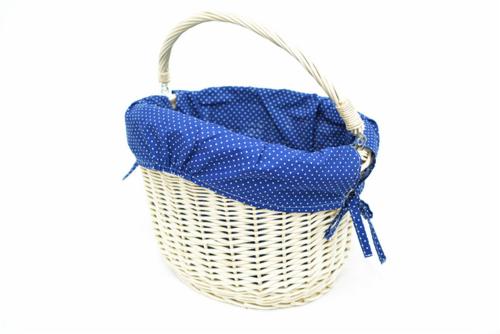 Owalny, wiklinowy koszyk z uchwytem, wyłożony granatowym materiałem w białe groszki, zawiązanym na kokardkę, na białym tle.