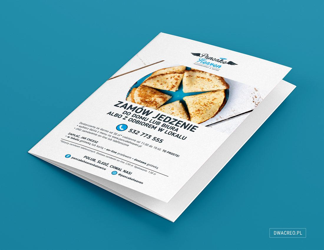Biała broszura reklamowa restauracji Pancake Heaven z grafiką naleśników na niebieskim talerzu i informacjami o dostawie, leżąca na niebieskim tle.