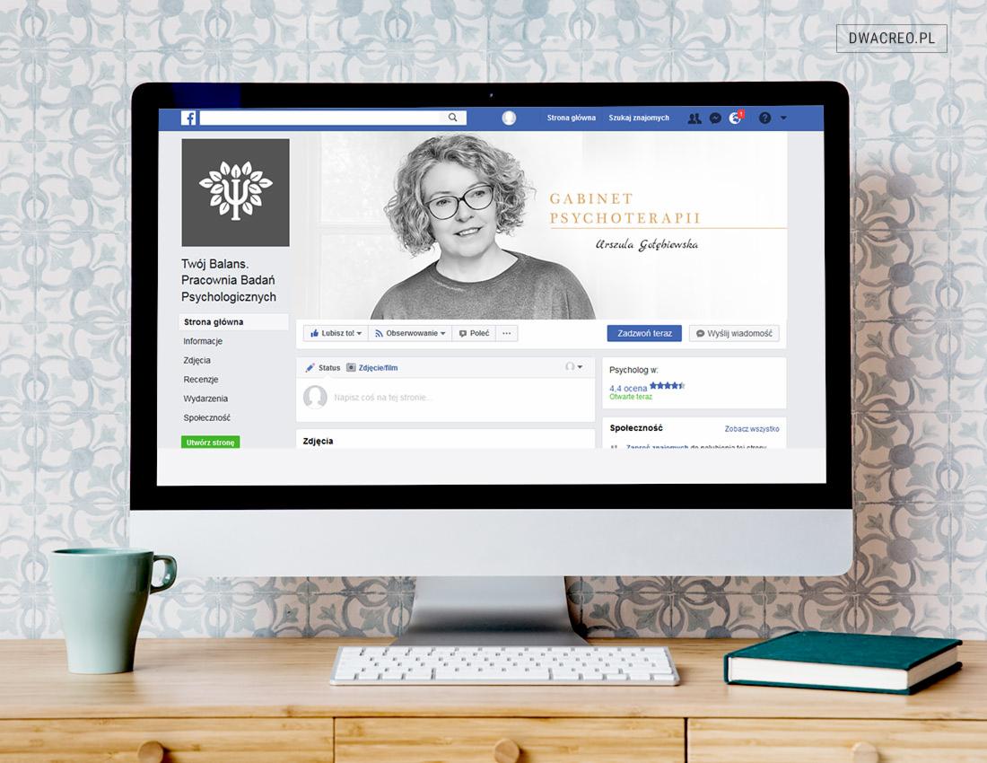 Ekran komputera iMac z wyświetloną stroną na Facebooku Gabinetu Psychoterapii Urszuli Gołębiewskiej, ustawiony na drewnianym biurku obok zielonego kubka i książki na tle wzorzystej ściany.