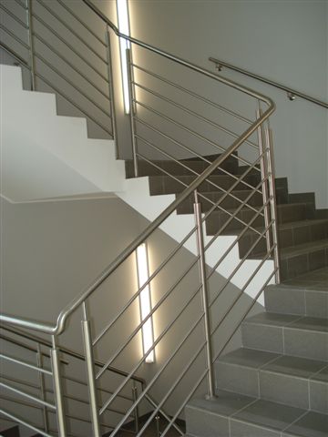 Schody wyłożone szarą płytką z nowoczesną balustradą ze stali nierdzewnej, oświetlone pionową lampą ścienną.