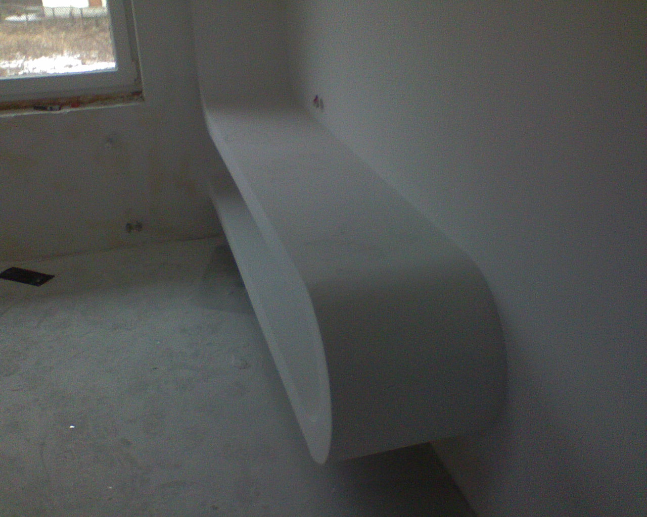 Niedokończona, zaokrąglona półka z kartongipsu na ścianie w trakcie remontu w Częstochowie, widoczna surowa podłoga i okno.