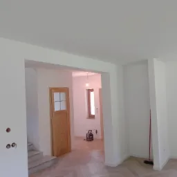 Świeżo pomalowane na biało wnętrze z drewnianą stolarką, widoczne gniazdka elektryczne bez osprzętu i podłoga w jodełkę.