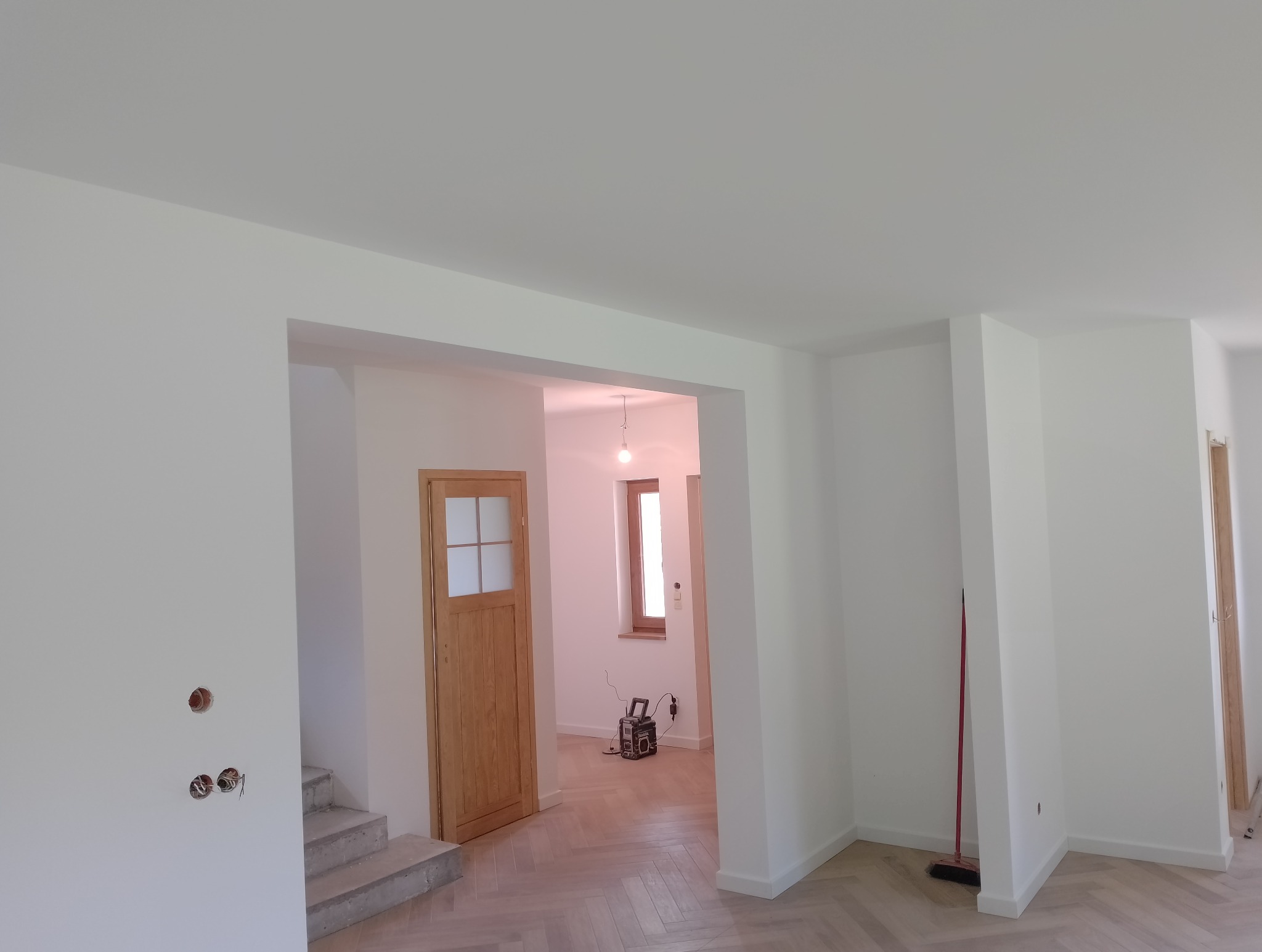 Świeżo pomalowane na biało wnętrze z drewnianą stolarką, widoczne gniazdka elektryczne bez osprzętu i podłoga w jodełkę.