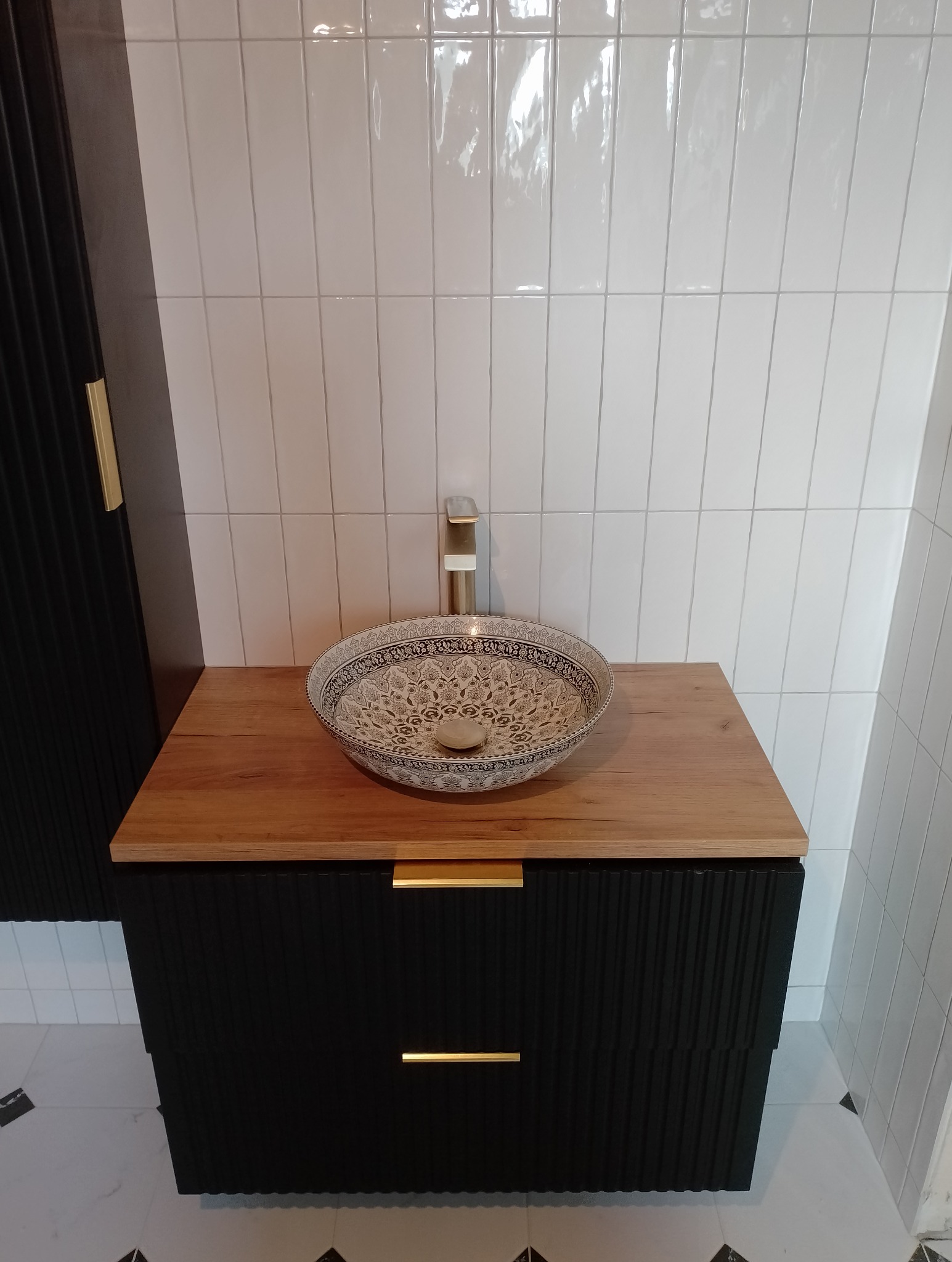 Umywalka nablatowa w etniczne wzory na drewnianym blacie szafki w łazience w Łapszach Niżnych, białe pionowe płytki na ścianie.