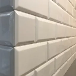 Białe i szare, błyszczące płytki typu cegiełka ułożone na ścianie w narożniku łazienki, widok z bliska.