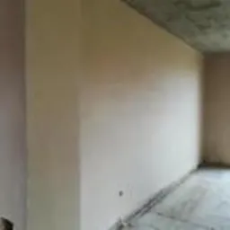 Świeżo nałożony, gładki tynk na ścianie w surowym wnętrzu z widocznym betonowym sufitem i oknem bez wykończenia.