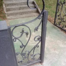 Metalowa brama z dekoracyjnymi elementami roślinnymi, prowadząca do schodów.