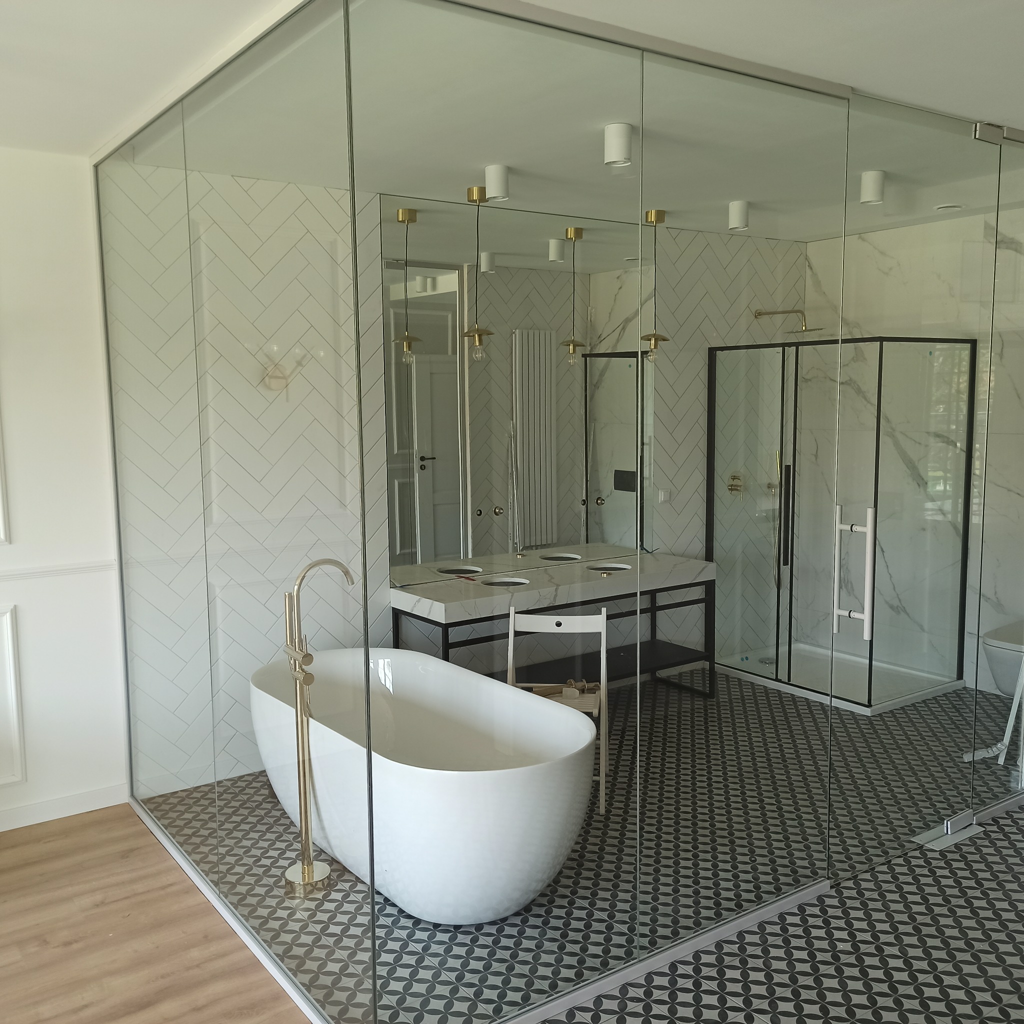 Nowoczesna łazienka w Sokołowie Podlaskim z kabiną prysznicową i wanną wolnostojącą, oddzielona szklaną balustradą, widoczne płytki w geometryczne wzory i biała armatura.