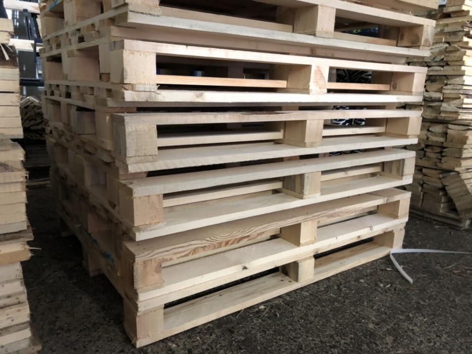 Stos jasnych, surowych palet drewnianych ułożonych jedna na drugiej, widoczne sęki i naturalny rysunek drewna, z białym sznurkiem zabezpieczającym na dole.