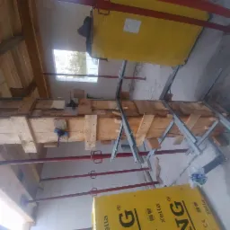 Szare fundamenty w trakcie wylewania, drewniane szalunki wzmocnione metalowymi profilami i czerwonymi stemplami, widoczne bloczki Ytong i okno w tle.