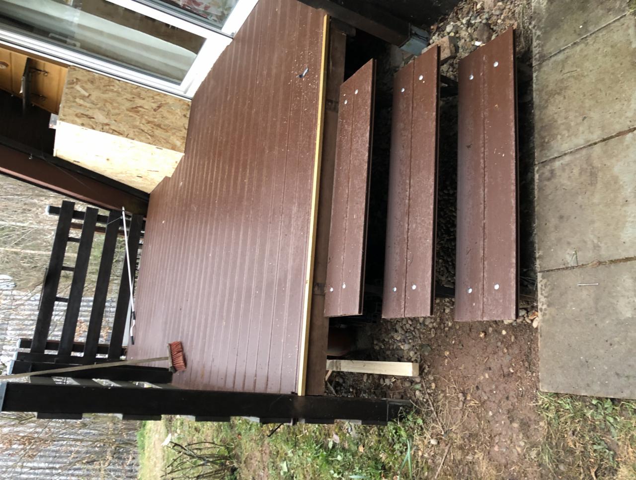 Montaż brązowego tarasu kompozytowego z widocznymi schodami i częścią konstrukcji domu w tle, widoczna szczotka do zamiatania