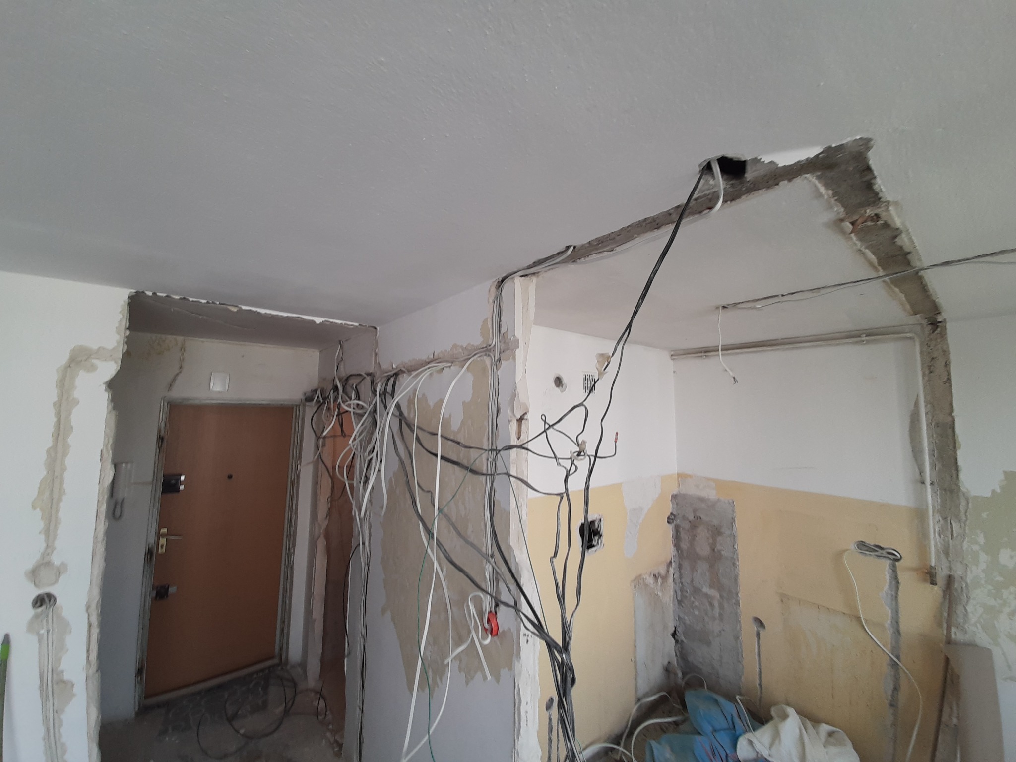 Wnętrze w trakcie remontu z widocznymi przewodami elektrycznymi wystającymi ze ścian i sufitu, ściany częściowo otynkowane, widoczne ślady po kuciu.