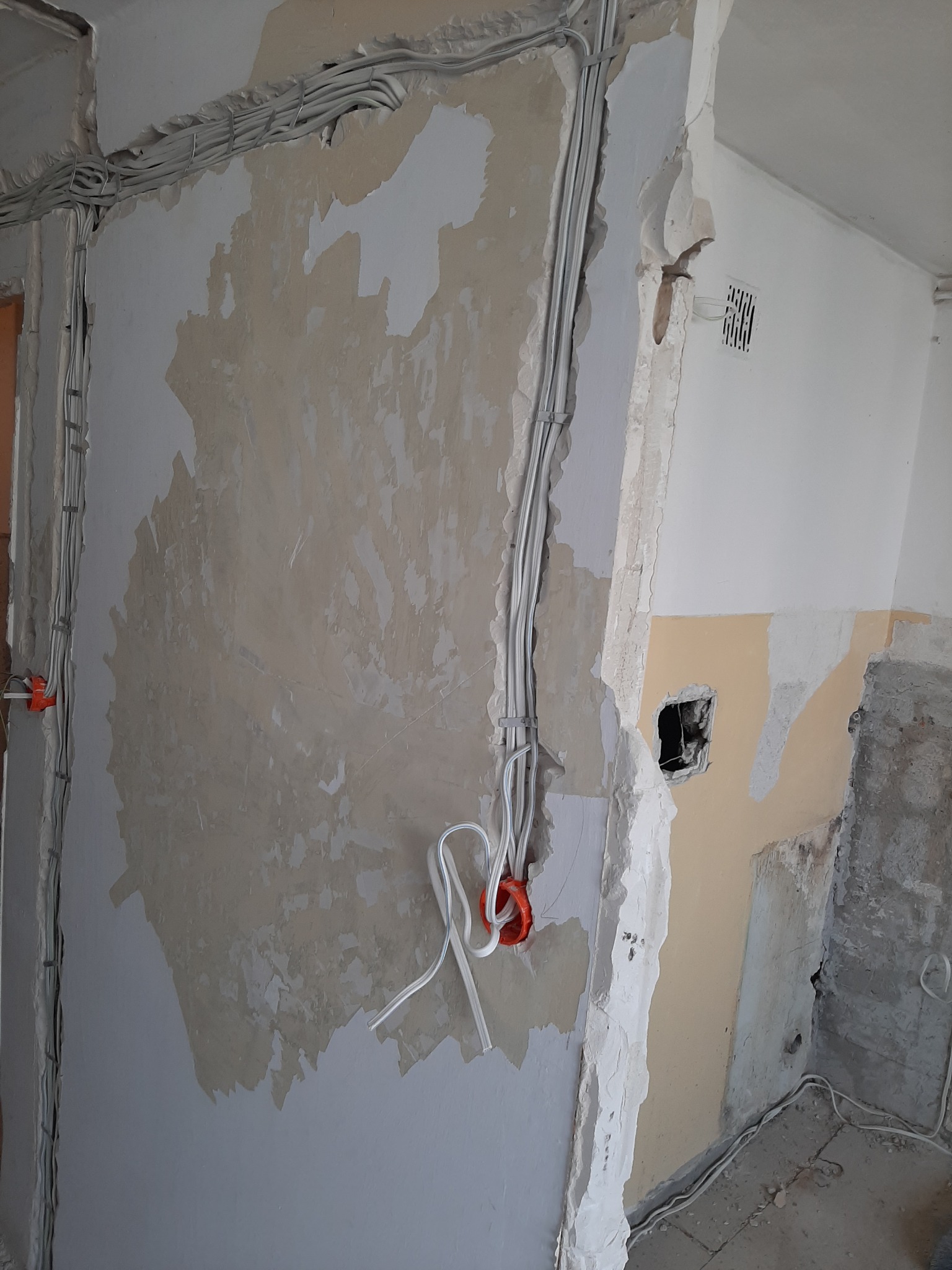 Instalacja elektryczna w trakcie remontu: widoczne kable prowadzone po ścianie, puszka elektryczna z wystającymi przewodami, fragment ściany z resztkami starej farby i tynku.