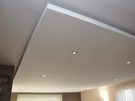 Gładki, biały sufit podwieszany z wbudowanymi, kwadratowymi lampami LED, wykończony listwą przypodłogową, widok z dołu.