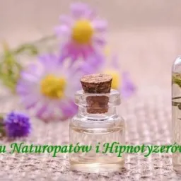 Dwie szklane buteleczki z korkami, jedna z gałązką w środku, ustawione na tle rozmytych fioletowych kwiatów i zielonego logo Cechu Naturopatów i Hipnotyzerów.