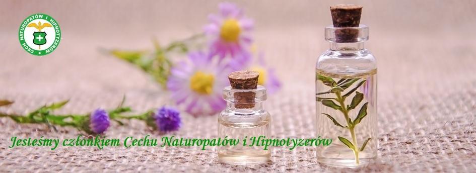 Dwie szklane buteleczki z korkami, jedna z gałązką w środku, ustawione na tle rozmytych fioletowych kwiatów i zielonego logo Cechu Naturopatów i Hipnotyzerów.