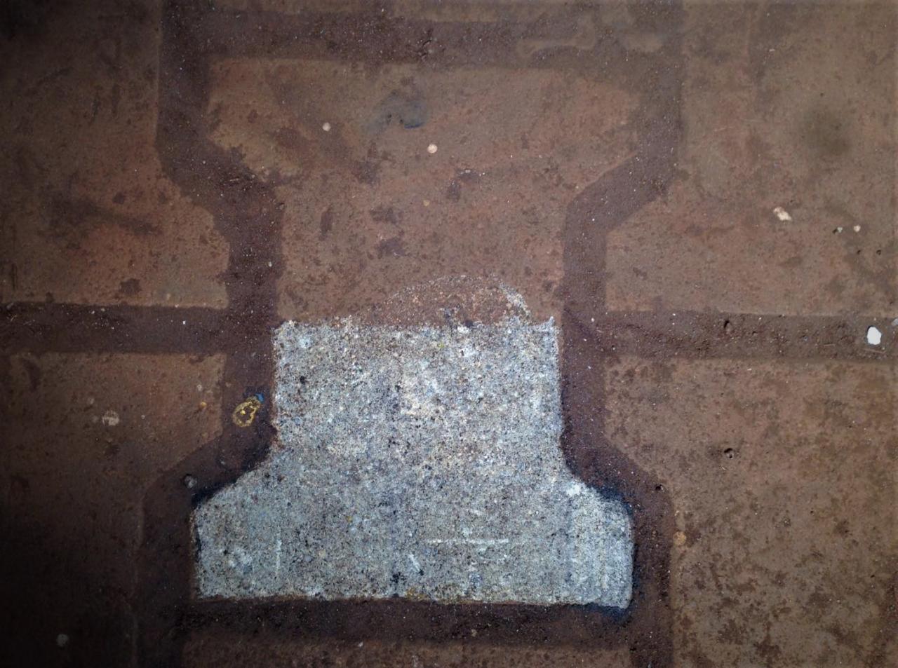 Fragment kostki brukowej po częściowym wyczyszczeniu, widoczne ślady brudu i wody w fugach.