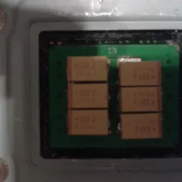 Zbliżenie na płytkę drukowaną z układem kondensatorów oznaczonych +337J, umieszczonych w dwóch kolumnach. Widoczny napis C79 na zielonej powierzchni płytki. Płytka otoczona czarną ramką, a całość...