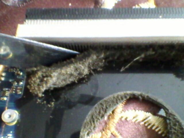 Detail laptopa z nagromadzonym kurzem wewnątrz, czyszczony ostrym narzędziem, widoczne elementy płyty głównej i wentylator.