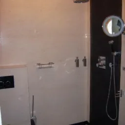 Nowoczesna kabina prysznicowa z deszczownicą, panelem w kolorze ciemnego brązu, podświetlanym lustrem i beżowymi płytkami na ścianach.