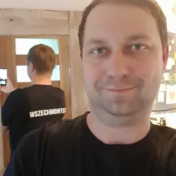 Mężczyzna w czarnej koszulce z logo firmy Wszechmonter, robiący sobie selfie w lustrze.