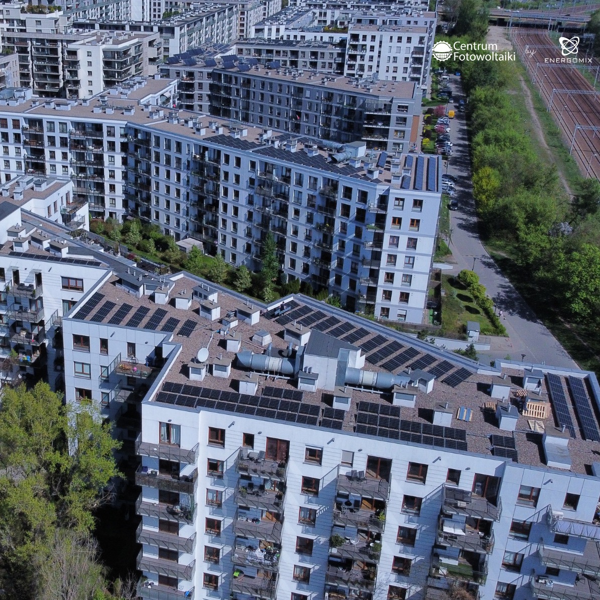 Panele słoneczne na dachach bloków mieszkalnych, widok z góry. Instalacja fotowoltaiczna z bliska na tle zabudowy miejskiej i zieleni.