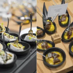 Dwa rodzaje przystawek w czarnych naczyniach: po lewej roladki z białego ciasta z zielonym farszem i widelczykami, po prawej kawałki ryby w żółtym sosie z posypką na drewnianej desce.