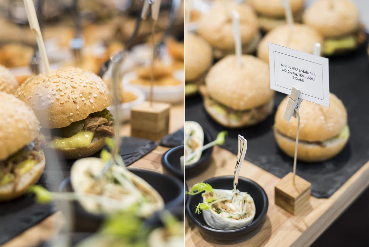 Mini burgery z szarpaną wołowiną, remuladą i piklami, oraz roladki z farszem w czarnych miseczkach, prezentowane na drewnianej desce podczas cateringu.