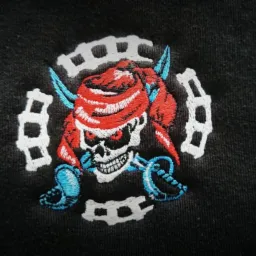 Czarna koszulka z wyhaftowanym kolorowym motywem pirackiej czaszki z szablami na tle białego ornamentu