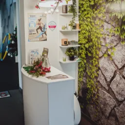 Recepcja w jasnym wnętrzu, ozdobiona roślinami i dekoracjami świątecznymi, plakat z motywem sportowym w tle, nowoczesne oświetlenie.