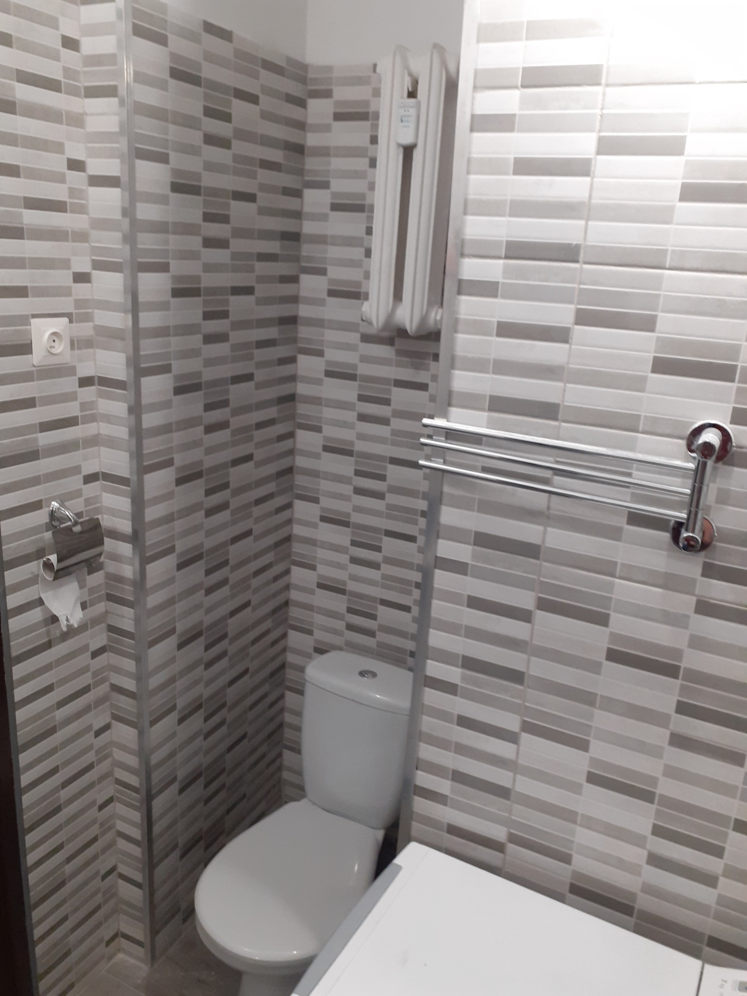 Wykończona łazienka z poziomymi, szaro-białymi płytkami, białą toaletą, grzejnikiem drabinkowym i uchwytem na ręczniki.