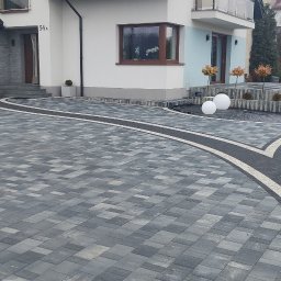 JAKUB GŁĄB PERFEKT-BRUK - Elegancka posesja z szarej kostki brukowej, z białymi obrzeżami i dekoracyjnymi kulami. Widok na dom z garażem i schodami.