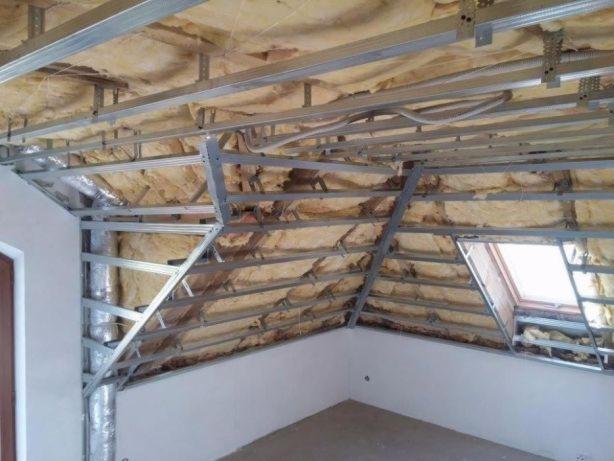 Ocieplone poddasze z widoczną konstrukcją metalową i oknem dachowym przed wykończeniem płytami gipsowymi.