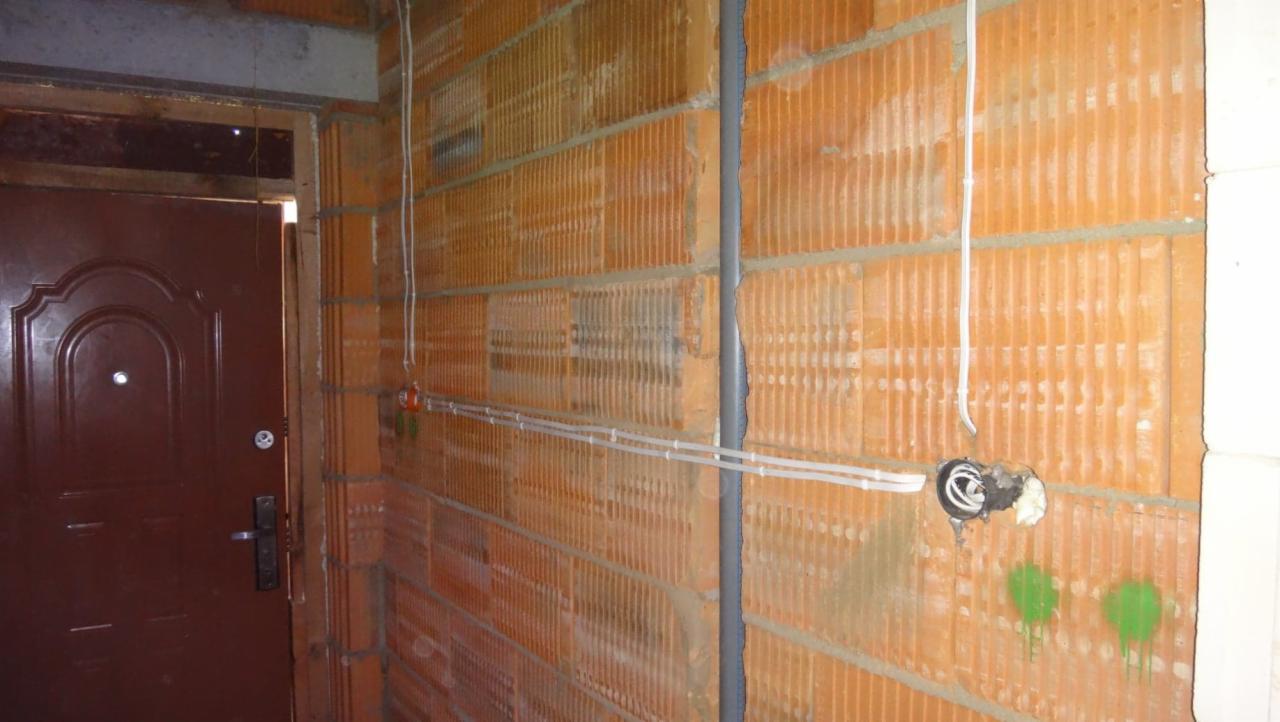 Murowana ściana z pustaków ceramicznych z widoczną instalacją elektryczną w trakcie montażu, przewody prowadzone wzdłuż ściany i puszka instalacyjna z wystającymi przewodami.