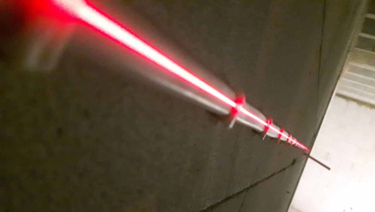 Ustawianie poziomu za pomocą lasera na szarej, betonowej ścianie w trakcie prac instalacyjnych.