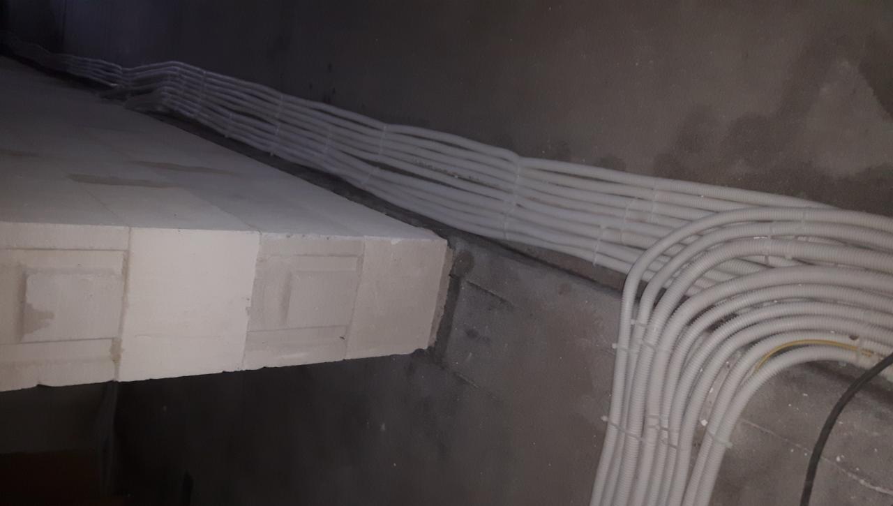 Pęki białych rur karbowanych ułożone równolegle wzdłuż surowej, szarej ściany z betonu komórkowego, widoczne okablowanie elektryczne w trakcie instalacji.