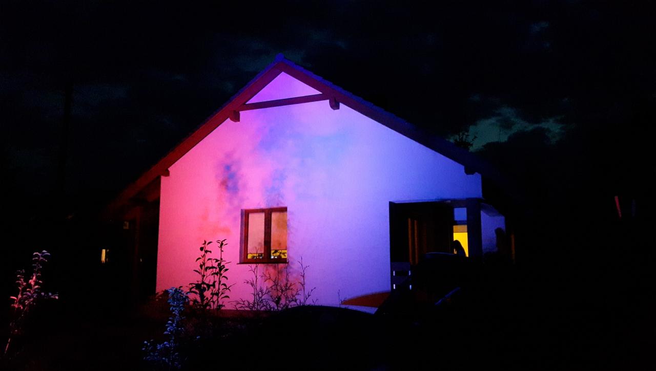 Dom jednorodzinny oświetlony nocą światłami w kolorach różu i błękitu, z ciemnym niebem w tle.