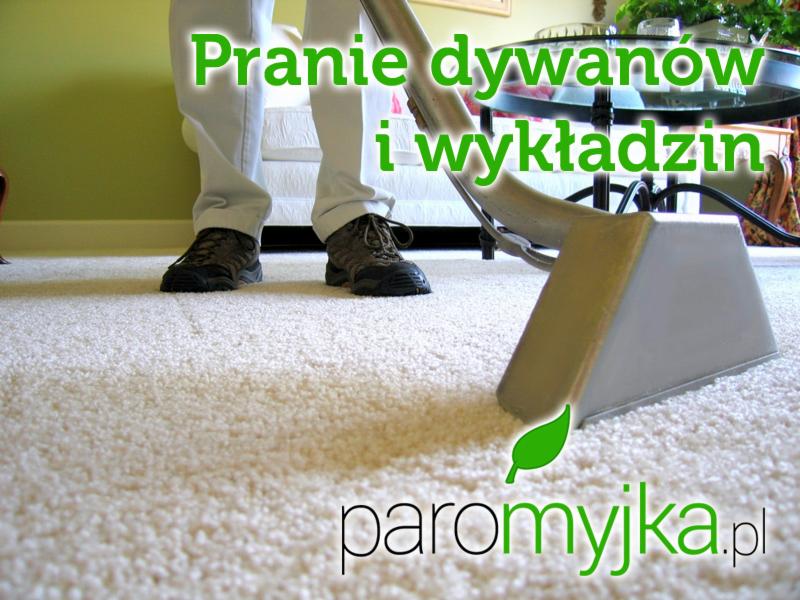 Dysza odkurzacza piorącego na jasnym, puszystym dywanie podczas czyszczenia, widoczne buty osoby obsługującej i fragment mebla w tle.