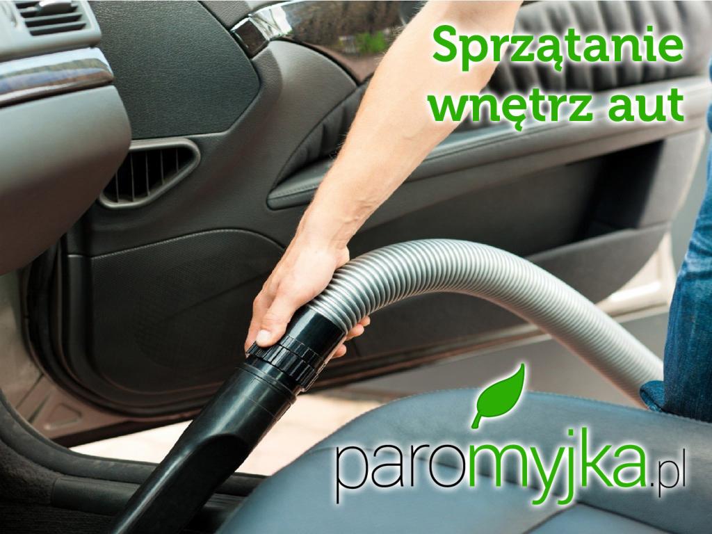 Czyszczenie tapicerki samochodowej odkurzaczem przemysłowym, widoczny fragment drzwi auta i ramię osoby wykonującej usługę.