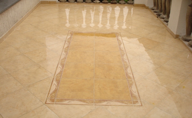 Beżowa podłoga z płytek ceramicznych ułożonych w karo, z centralnym prostokątnym wzorem obramowanym dekoracyjnym pasem.