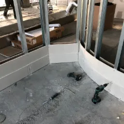 Montaż zakrzywionej ściany działowej z płyt gipsowo-kartonowych w Chełmnie, widoczne metalowe profile, płyty przykręcane wkrętarką, narzędzia na podłodze.